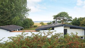 A white building with a sloped roof, a chimney, and a view of a body of water. - 4 Person Holiday Home in Tranekaer (Tranekaer)