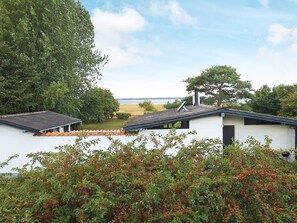 A white building with a sloped roof, a chimney, and a view of a body of water. - 4 Person Holiday Home in Tranekaer (Tranekaer)