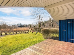 A wooden deck with a view of a garden, a blue door, and a swing set. - Superb Holiday Home in Hemmet near Sea (Hemmet)
