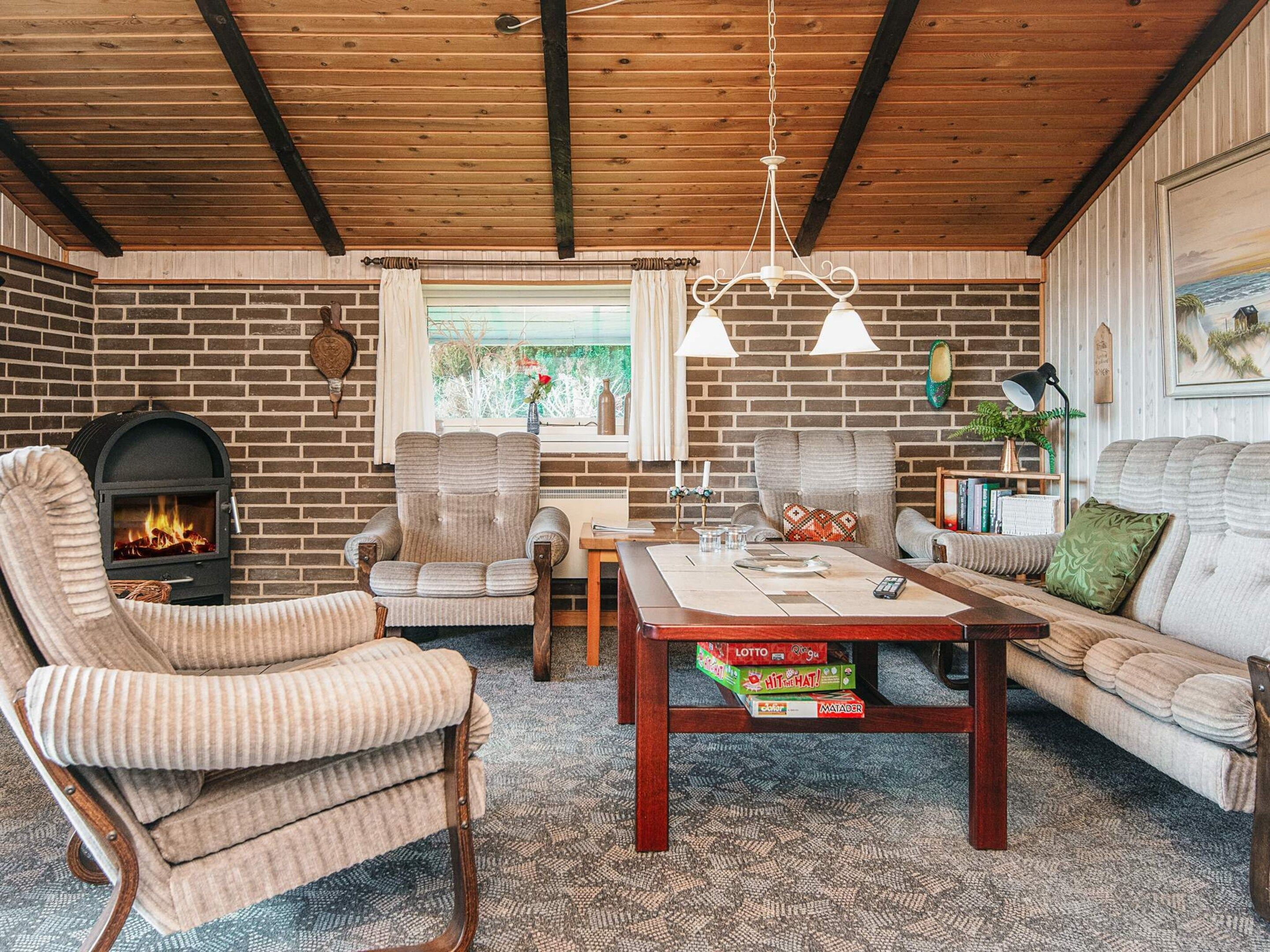 A cozy living room with a brick fireplace, wooden ceiling beams, and a comfortable seating area with a sofa and armchairs.