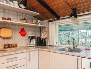 A kitchen with a wooden ceiling, a window with a view of trees, and various kitchen appliances and utensils. - Superb Holiday Home in Hemmet near Sea (Hemmet)