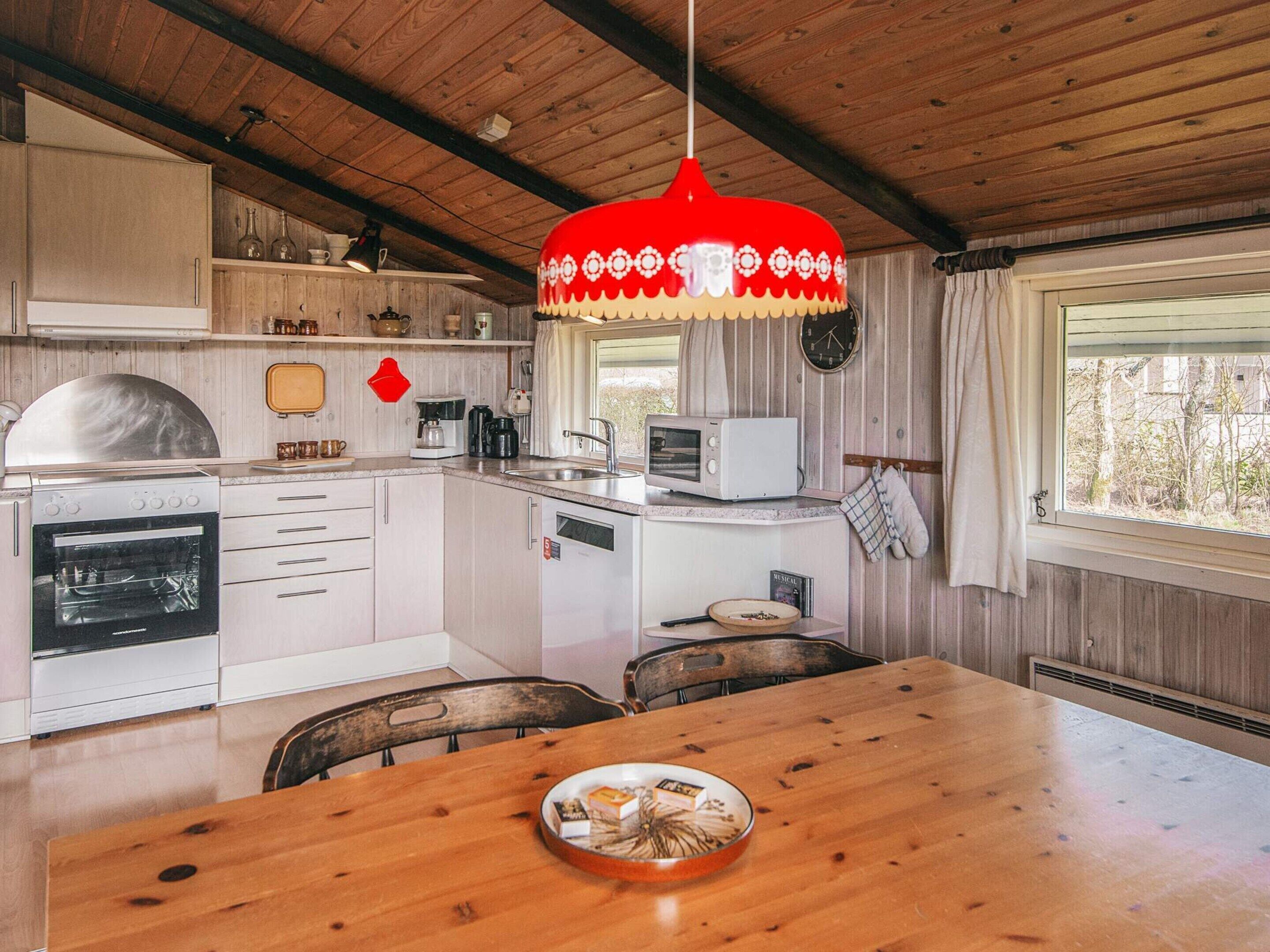 Una cocina con armarios de madera, estufa, microondas y una lámpara colgante roja.