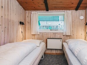 A small, cozy room with two single beds, a window with curtains, a wall-mounted heater, and a view of a building outside. - Superb Holiday Home in Hemmet near Sea (Hemmet)