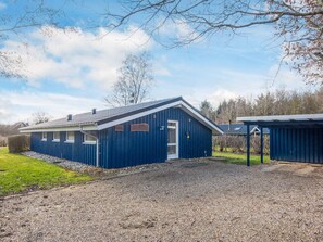 En blå byggnad med en grusuppfart och en liten trädgårdsyta.