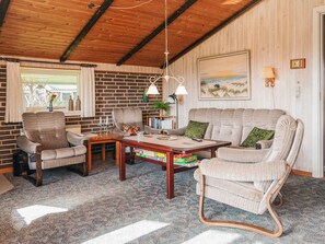 A cozy living room with a brick wall, wooden ceiling, and a large window. There are two armchairs, a sofa, and a coffee table with books and a lamp. - Superb Holiday Home in Hemmet near Sea (Hemmet)
