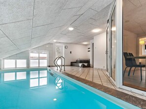 An indoor swimming pool with a tiled floor, a reception area with a counter and chairs, and a large window with frosted glass panels.