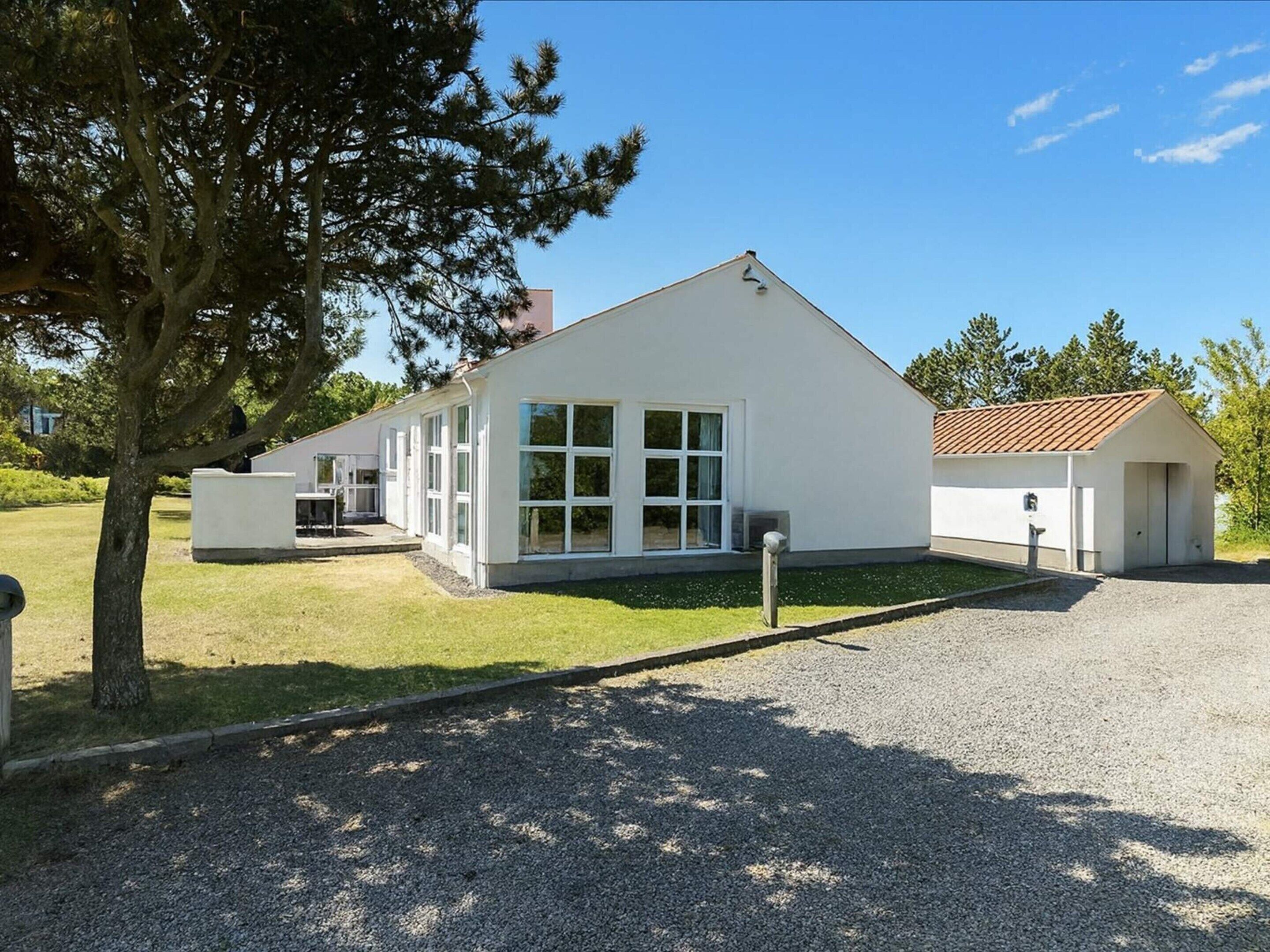 A modern building with a sloped roof, large windows, and a gravel driveway.