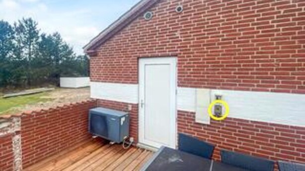 A brick building with a white door, a small outdoor area with a wooden deck, and a blue object on the deck.