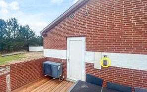 A brick building with a white door, a small outdoor area with a wooden deck, and a blue object on the deck.