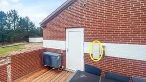 A brick building with a white door, a small outdoor area with a wooden deck, and a blue object on wheels.