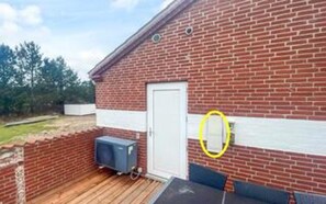 A brick building with a white door, a small outdoor area with a wooden deck, and a blue object on wheels.