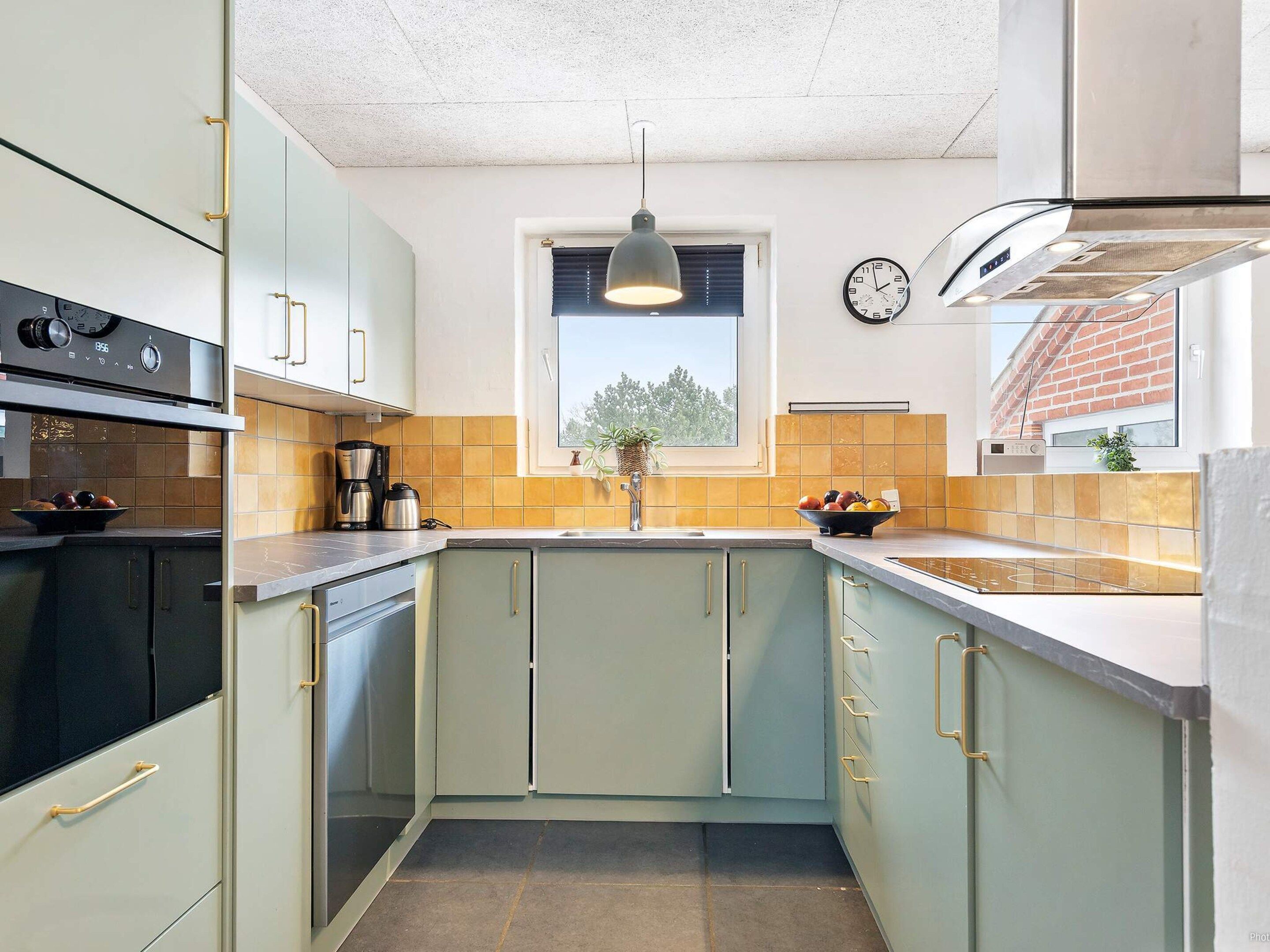A compact kitchen with light green cabinets, a black stove, and a window with a view of trees.