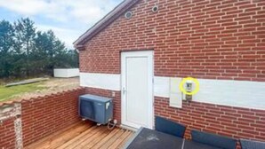 A brick building with a white door, a small outdoor area with a wooden deck, and a blue object on the deck.
