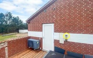 A brick building with a white door, a small outdoor area with a wooden deck, and a blue object on the deck.