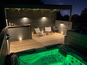 A hot tub area with a wooden deck, two chairs, and a bar area with glasses.