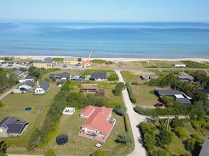 An aerial view of a coastal residential area with houses, a beach, and a road leading to the sea.
