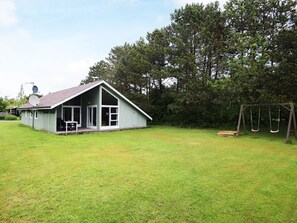 A single-story house with a porch, a swing set, and a grassy yard.