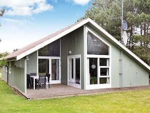 Un edificio de una sola planta con techo inclinado, grandes ventanales y un patio cubierto con una mesa y sillas.