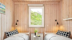 Una habitación pequeña y acogedora con dos camas, una ventana que da a zonas verdes y una mesita con una planta.