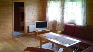 L’intérieur d’un chalet en bois, avec un plancher en bois, une télévision posée sur une table, un canapé et un banc.