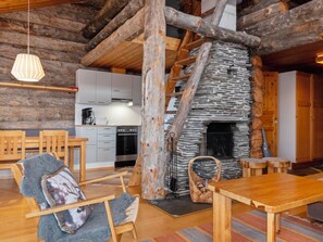 A rustic interior with a stone fireplace, wooden furniture, and a kitchen in the background.