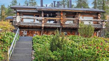 A log cabin with a wooden staircase leading to the entrance, surrounded by lush greenery.