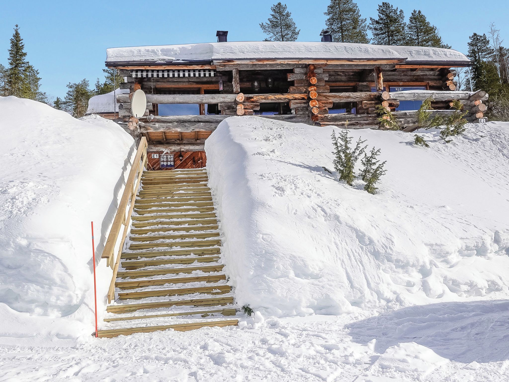 A log cabin with a wooden staircase leading to a door, surrounded by snow.