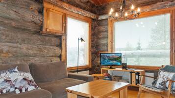L’intérieur d’un chalet accueillant, avec un revêtement mural en bois, un canapé, une table, un bureau et un écran d’ordinateur.