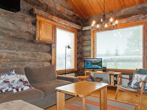 A cozy cabin interior with a wooden interior, a sofa, a table, a desk, and a computer monitor.