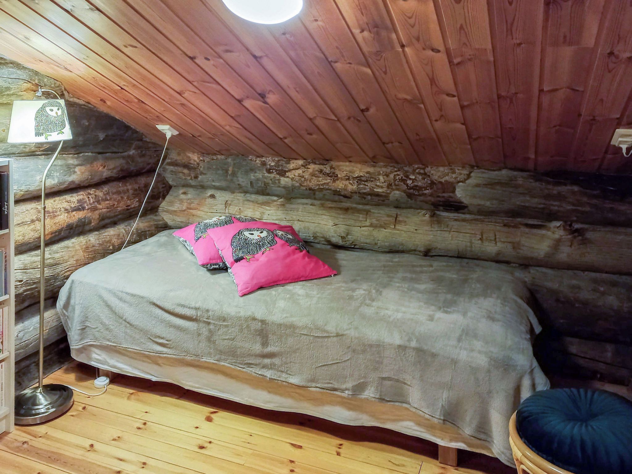 A cozy log cabin room with a bed, a lamp, and a wooden floor.