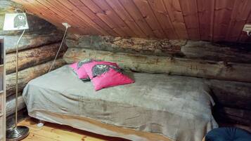 A cozy log cabin room with a bed, a lamp, and a wooden floor.