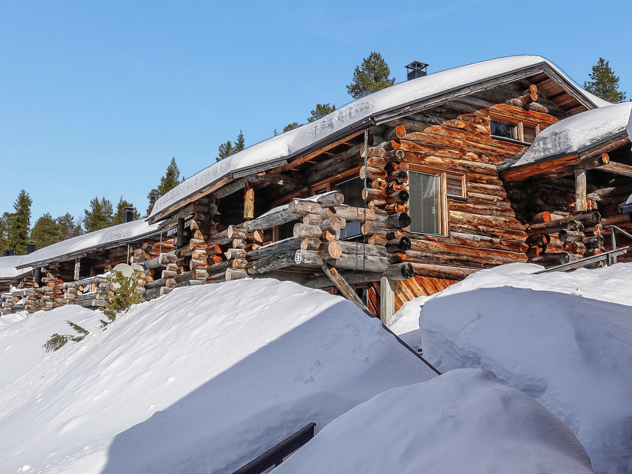 Una cabaña de troncos con techo nevado, rodeada de nieve.