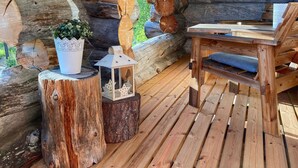 Une terrasse en bois rustique, avec une chaise et une table en bois, entourée de troncs d’arbres et d’une petite lanterne.
