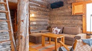 L’intérieur d’une cabane en rondins, avec un canapé, une table et une chaise recouverte d’une couverture.