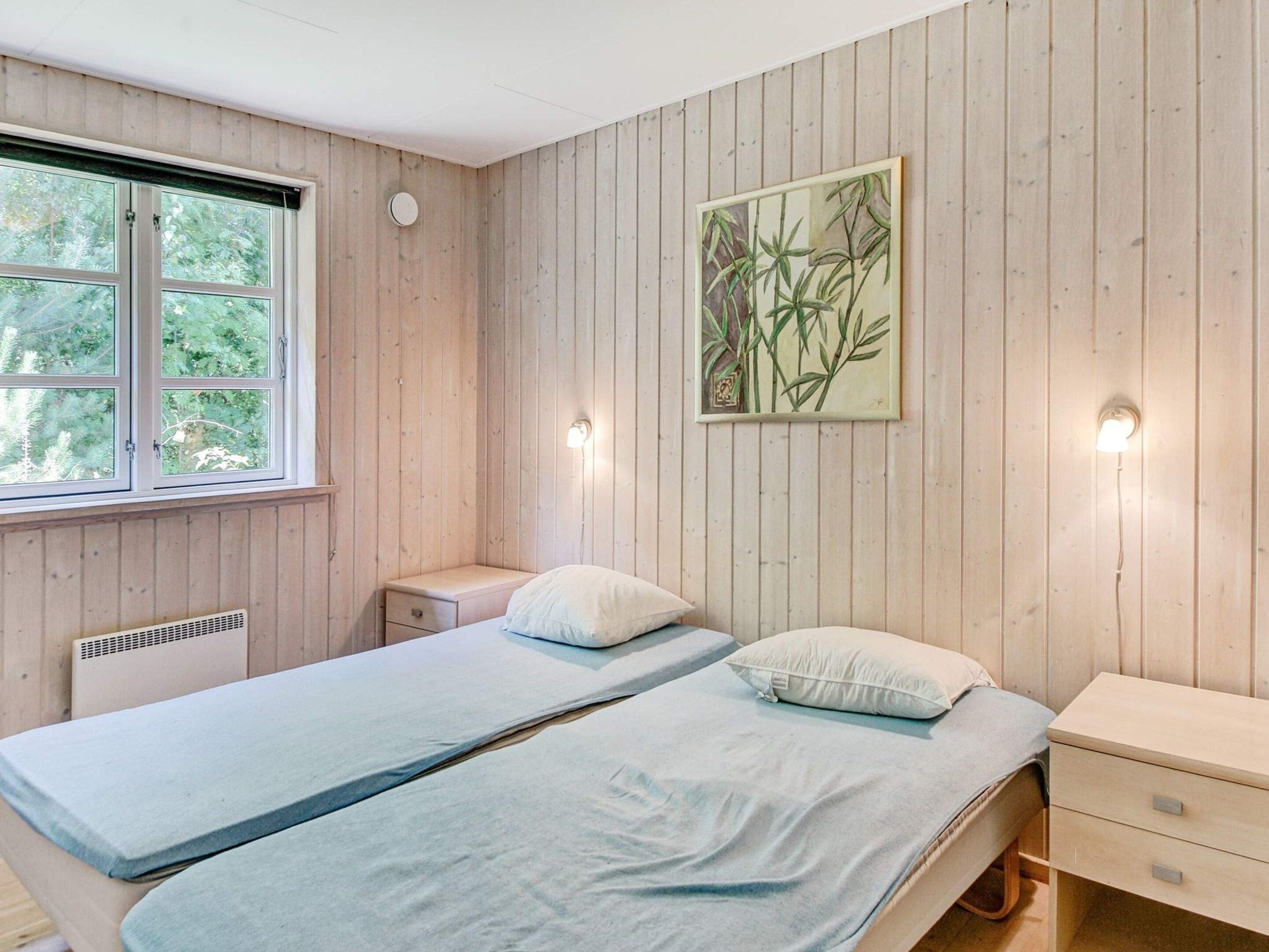A room with two beds, a window, a radiator, and a wall-mounted light fixture.