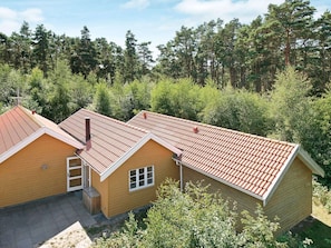 Een houten huis met twee verdiepingen en een rood dak, omgeven door een dicht bos.