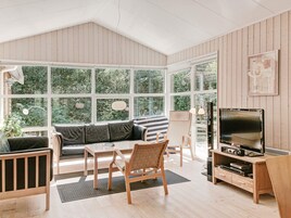 Una habitación amplia con techo alto, ventanas grandes, un sofá, una mesa de comedor, sillas, un televisor y un mueble de madera.