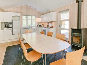 A modern kitchen with white cabinets, a dining table, chairs, a stove, and a window. - 5 Star Holiday Home in Aakirkeby (Akirkeby)