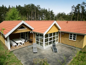 Een houten huis met twee verdiepingen, voorzien van een terras met tuinmeubilair en een groot raam.