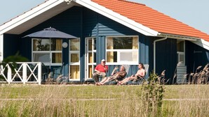 Une maison avec un toit rouge, une antenne parabolique et une véranda avec des chaises.