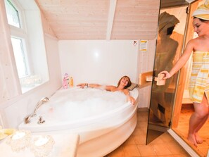 A person relaxing in a large bathtub with a window and a wooden ceiling. - Holiday Home in Otterndorf (Otterndorf)
