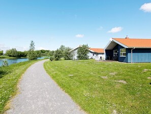 A pathway leading to a blue building with a red roof, surrounded by greenery and a body of water. - Holiday Home in Otterndorf (Otterndorf)