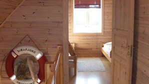 Interieur van een houten hutje met een stapelbed, een reddingsboei en een raam met jaloezieën.