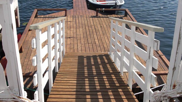 Een houten steiger die uitkomt bij een kleine witte boot die aan een steiger vastgemaakt is.