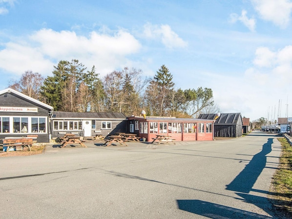 A waterfront area with buildings, picnic tables, and a dock with boats. - 5 Person Holiday Home in Hojslev (Hojslev)