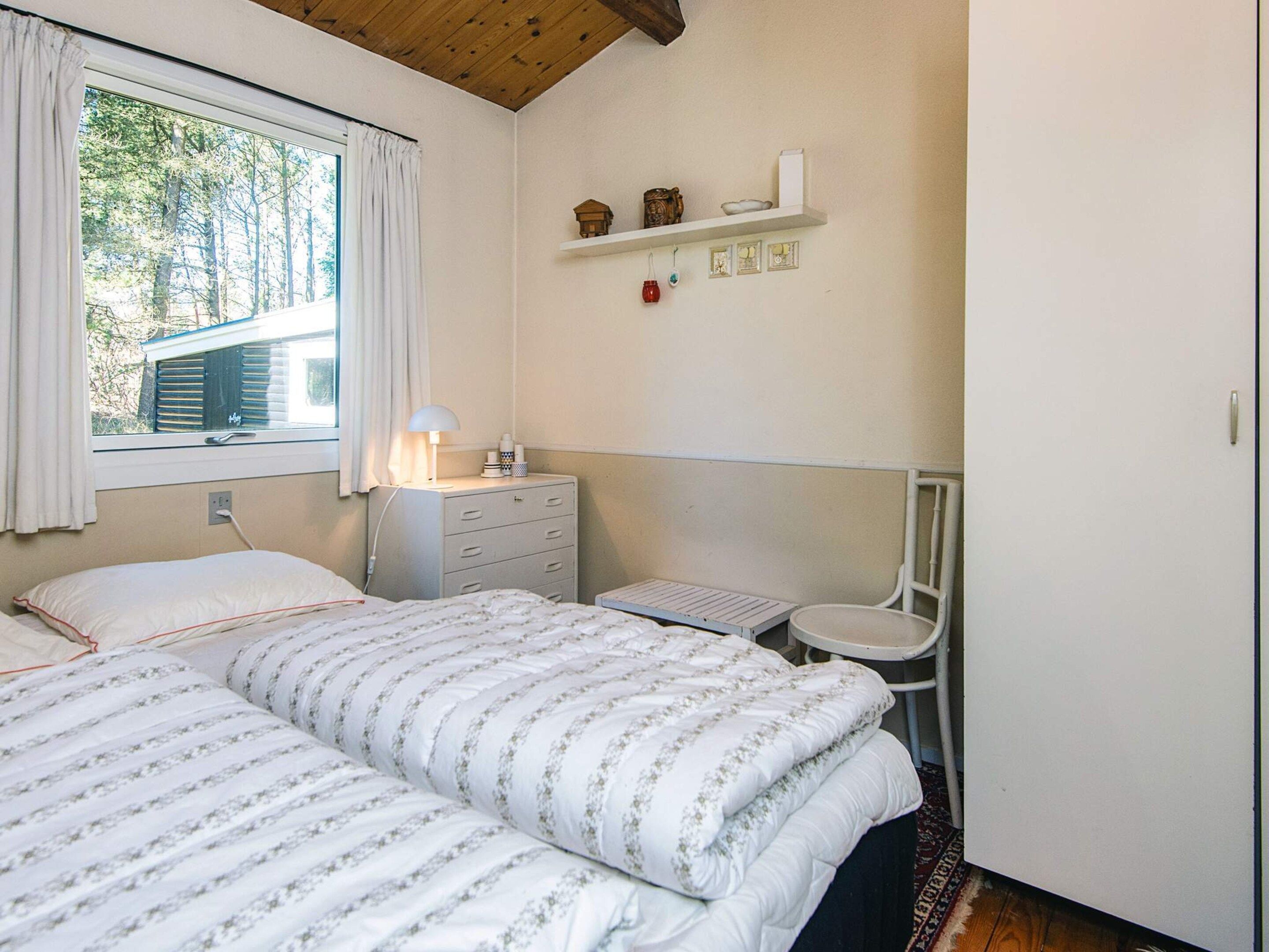 Ein Schlafzimmer mit einem Bett, einem Nachttisch, einem Sessel und einem Regal mit Dekoration.