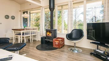 Una sala de estar acogedora con una estufa de leña, un comedor con mesa y sillas, y un televisor sobre un mueble.