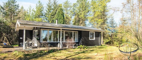 A modern cabin with a covered patio, large windows, and a natural forest backdrop.