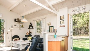 A cozy room with a dining table, a black leather chair, a small kitchen area, and a view of the outdoors. - 5 Person Holiday Home in Hojslev (Hojslev)