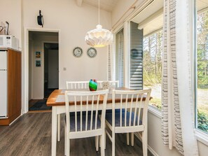 A dining area with a wooden table and white chairs, a hanging light fixture, and a view of the outdoors through a window with blinds. - 5 Person Holiday Home in Hojslev (Hojslev)